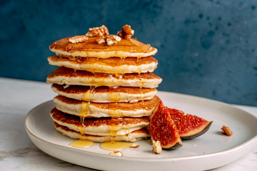 Stack of fluffy pancakes topped with melting butter and drizzled with maple syrup